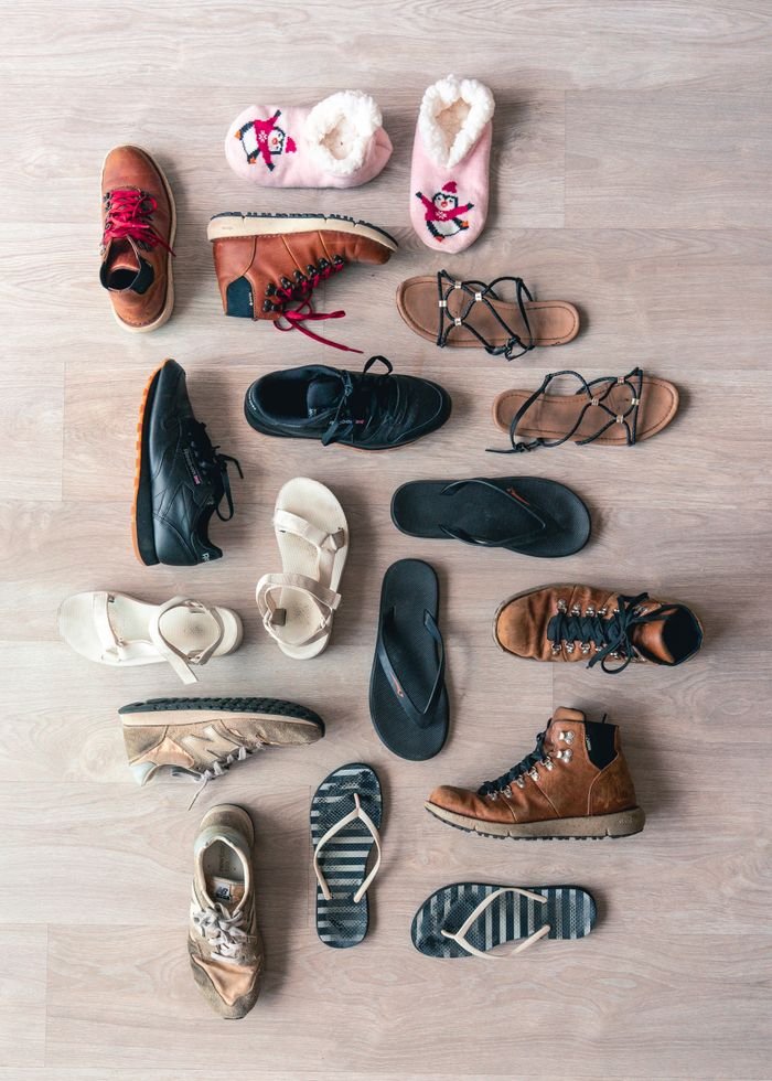 Services A diverse collection of footwear including boots, sandals, and slippers arranged in a flat lay on a wooden surface.